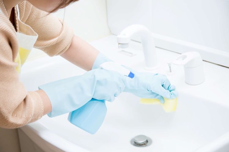ゴム手袋をはめた女性がスポンジで洗面台を掃除している