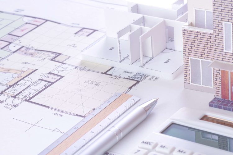 住宅の模型と図面、定規やボールペン、電卓が並べられている