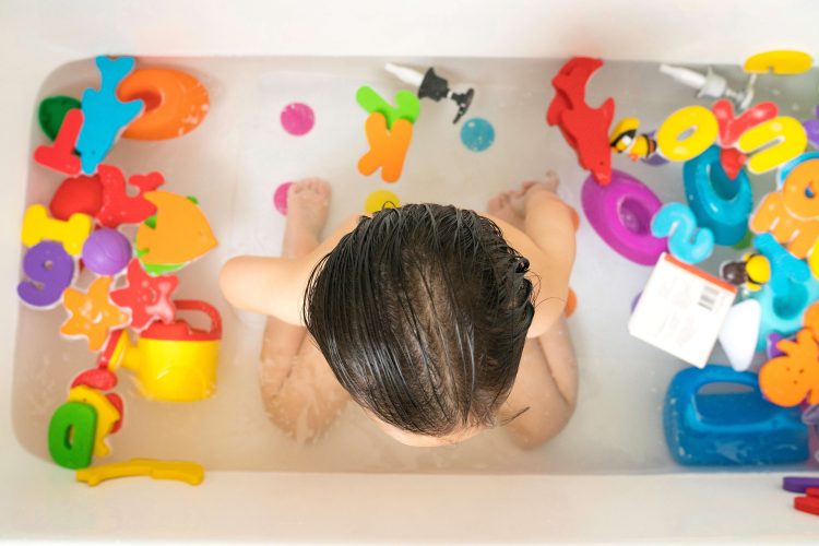 カラフルなおもちゃの数々と一緒に浴槽に入る子供を上から撮影した写真