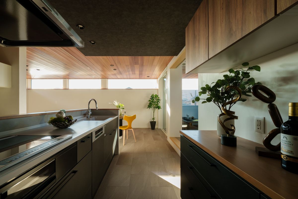 木目張りの天井と高窓からの自然光が特徴的な、黒いキャビネットを備えたモダンなキッチンとダイニングルームの内観デザイン。
