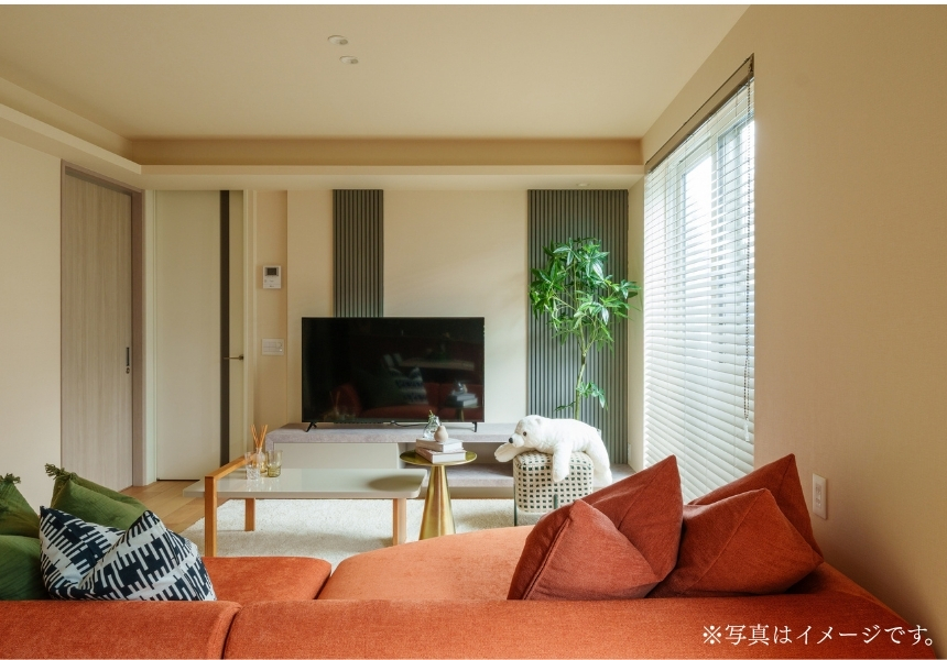 米沢市の完成邸見学会・リビングの内観・縦格子のテレビ背面壁とオレンジのソファを配したベージュ基調の空間