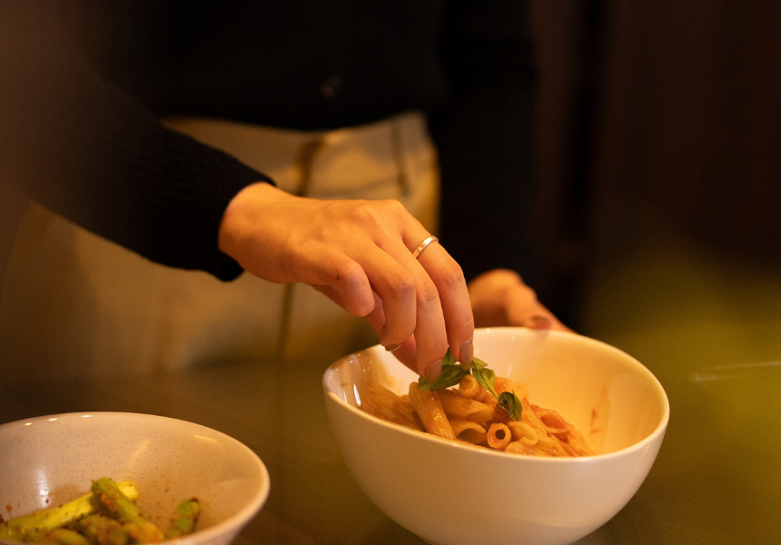注文住宅での暮らしのイメージ・ダイニングでペンネのトマトパスタにバジルを添える食卓の準備風景